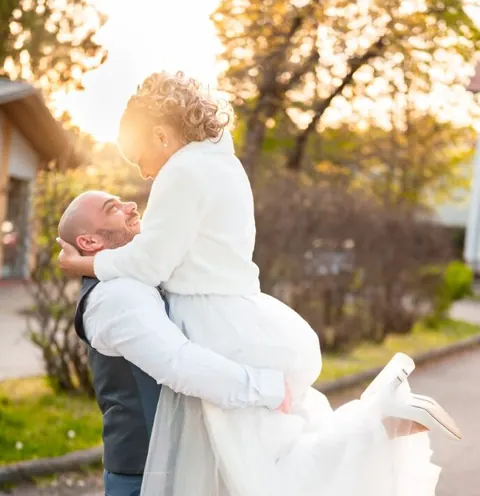 Vőlegény a karjában tartja a menyasszonyt egy őszi kertben