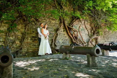 Menyasszony és vőlegény borostyános téglafal és régi ágyúk előtt