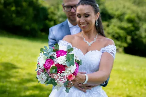 Menyasszony és vőlegény színes menyasszonyi csokorral egy kertben